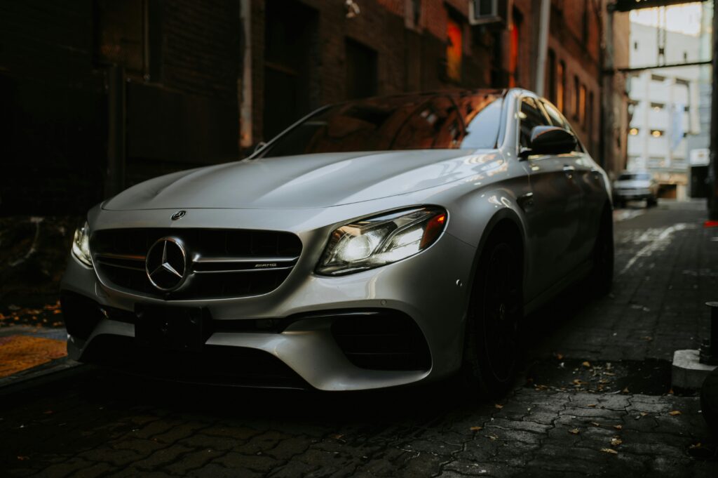 Close-up of a silver Mercedes parked in a dimly lit narrow alley, showcasing urban elegance.